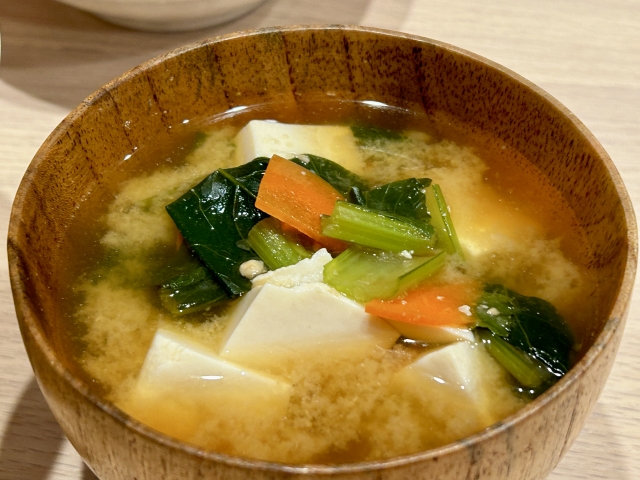 Tofu cubes in miso soup with leafy greens and carrot, showing how tofu absorbs and softens Japanese flavors.