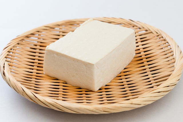 A firm block of tofu placed on a bamboo basket, showing tofu as a simple soybean food commonly used in Japanese cooking.
