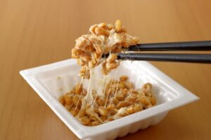 Natto being lifted with chopsticks from a small package, showing its sticky texture as a common Japanese breakfast food.