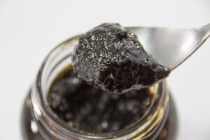 Dark nori tsukudani being lifted from a jar with a spoon, showing its soft, glossy, preserve-like texture.