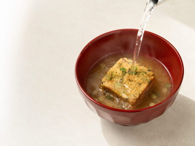 Hot water being poured over a freeze-dried instant miso soup cube in a red bowl.