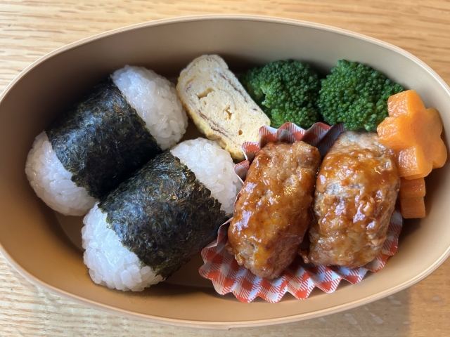 <img src="画像URL" alt="Two onigiri rice balls packed in a simple bento box as a portable everyday meal.">