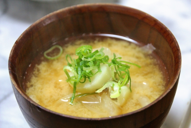 A bowl of miso soup with potatoes, cabbage, and sliced green onions in a wooden lacquer bowl.