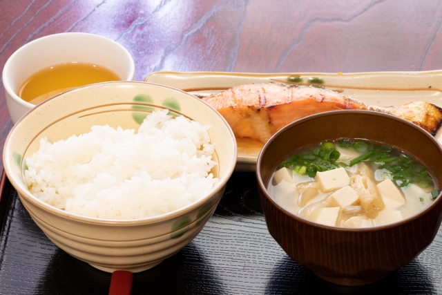 A Japanese breakfast with a bowl of rice, tofu miso soup, and grilled salmon, showing how rice and soup form the foundation of the meal.
