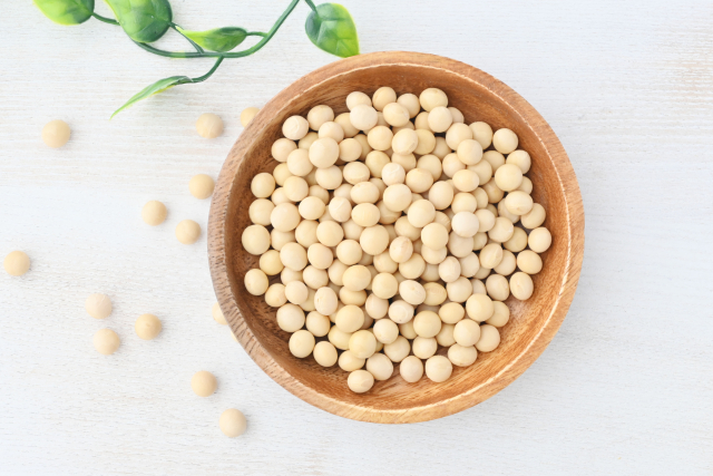 Dried soybeans in a wooden bowl on a light background.