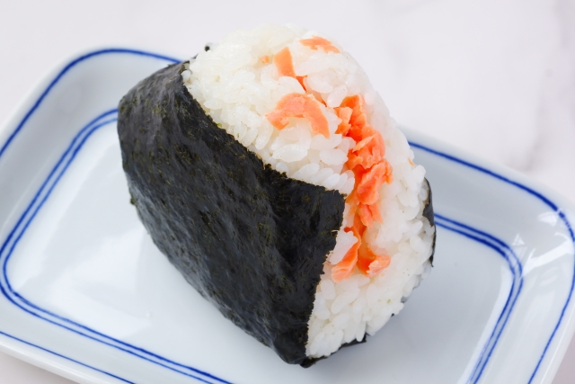 A salmon-filled Japanese onigiri wrapped in nori seaweed, showing the filling inside.