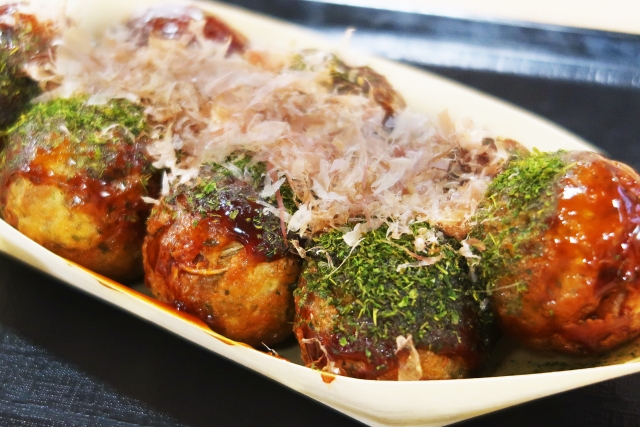 Takoyaki topped with aonori and bonito flakes, showing how finely crumbled green seaweed is used as an aromatic seasoning in Japan.