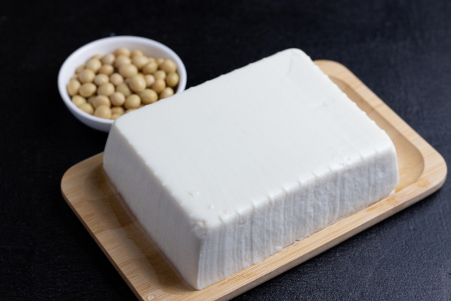 A block of fresh tofu displayed beside whole soybeans on a wooden tray.