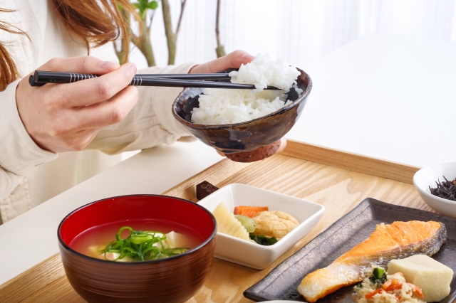 A person eating rice with a Japanese meal that includes grilled fish, miso soup, and a small serving of pickles, showing how tsukemono are eaten in small amounts throughout the meal.