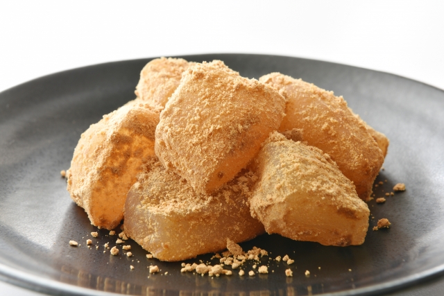 Warabi mochi dusted with kinako, a roasted soybean flour, served on a black plate.