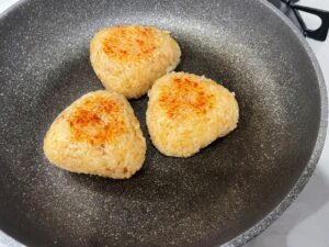 Homemade yaki onigiri in a frying pan, showing their lightly crisp browned surface.