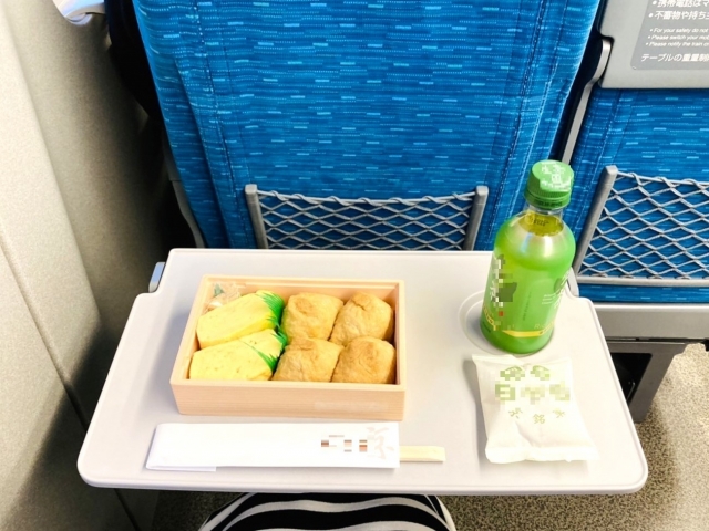 A Japanese bento meal with bottled green tea on a Shinkansen tray table.