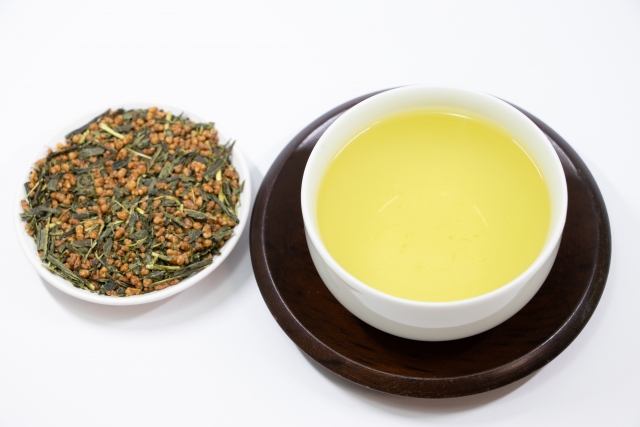 Genmaicha tea leaves blended with roasted rice beside a cup of pale green tea.