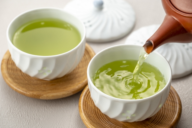 Bright green Japanese tea being poured from a teapot into a white teacup.