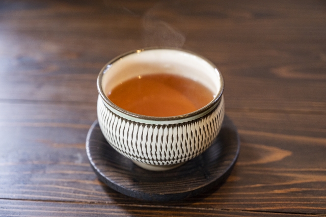 A steaming cup of amber-colored hojicha in a Japanese teacup on a wooden table
