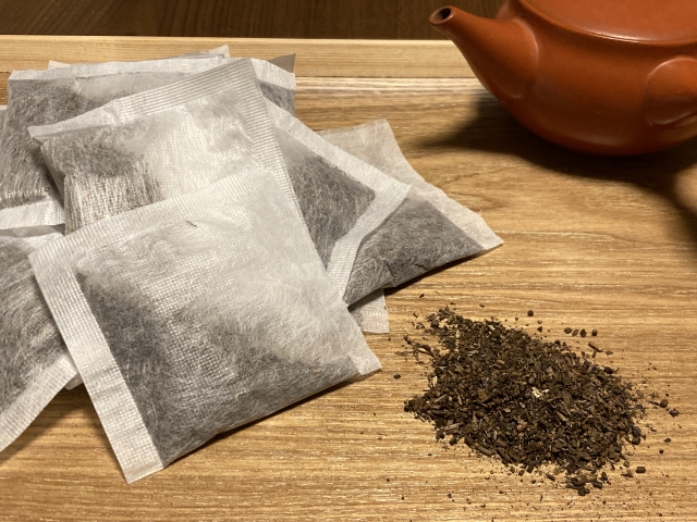 Hojicha tea bags and loose roasted tea leaves beside a Japanese teapot