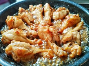 Chicken drumettes simmering in a bubbling teriyaki-style sauce as the liquid reduces.