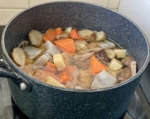Chikuzenni, a Japanese simmered dish with root vegetables and konjac, cooking in a pot of seasoned broth.