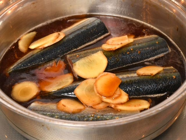Fish simmering in a soy sauce-based broth with sliced ginger, a common Japanese method for managing aroma.