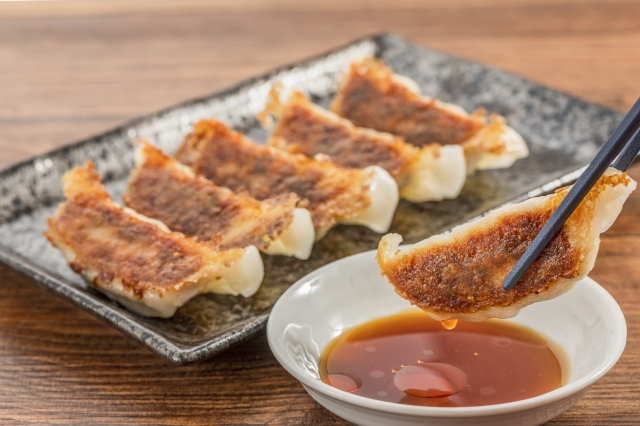 Japanese pan-fried gyoza being dipped into a small bowl of vinegar and soy sauce.