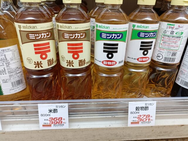 Mizkan rice vinegar and grain vinegar bottles displayed side by side in a Japanese supermarket.