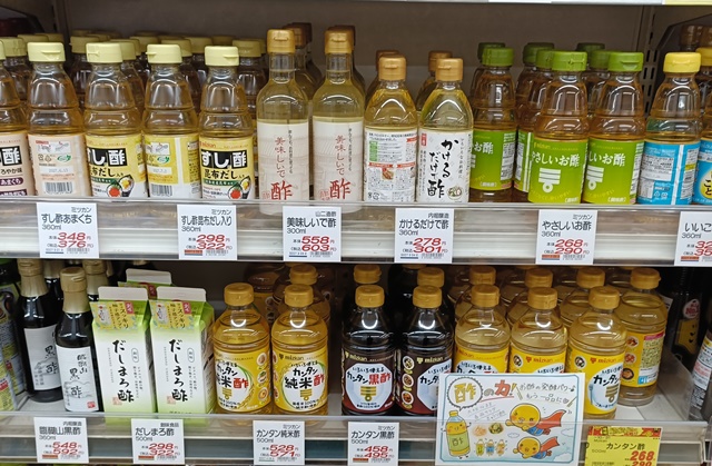 A Japanese supermarket shelf displaying many kinds of seasoned vinegars, including sushi vinegar, dashi-flavored vinegar, mild vinegar, and sweetened vinegar products.