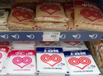 Japanese supermarket shelf displaying bags of jōhakutō white sugar, granulated sugar, and coarse brown sugar