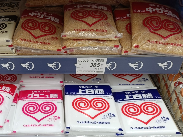 Japanese supermarket shelf displaying bags of jōhakutō white sugar, granulated sugar, and coarse brown sugar