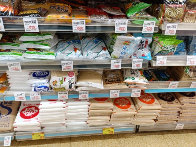 Japanese supermarket shelf displaying white sugar, granulated sugar, brown sugar, beet sugar, and rock sugar