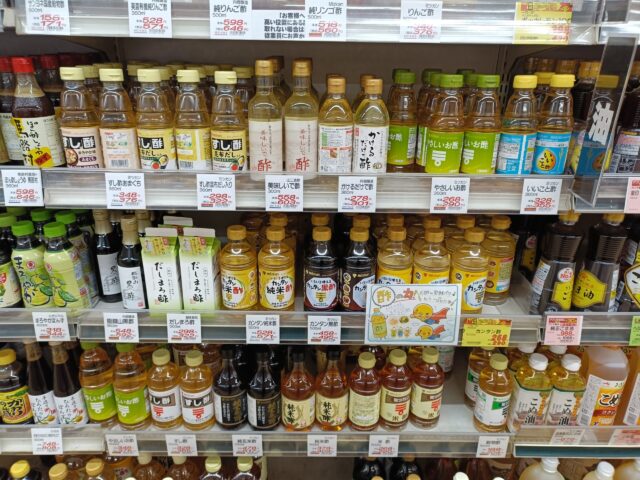 A Japanese supermarket shelf displaying rice vinegar, grain vinegar, black vinegar, and seasoned vinegar.