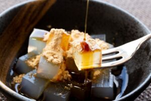 Cubes of Japanese kanten agar jelly topped with kinako soybean flour and drizzled with kuromitsu black sugar syrup