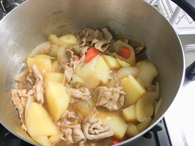 Nikujaga simmering in a pot with potatoes, onions, meat, and a seasoned cooking liquid.