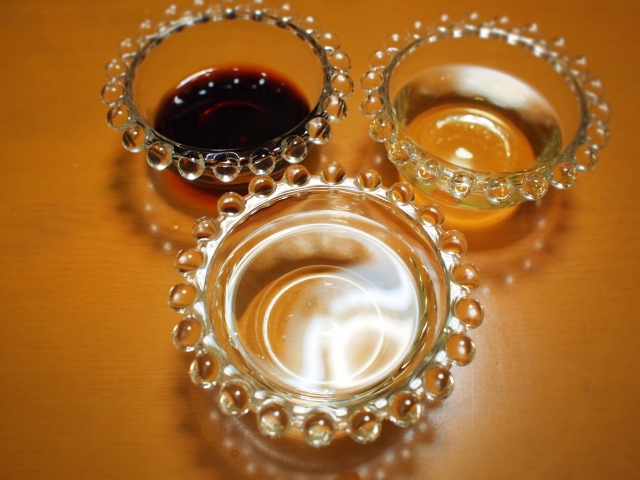 Three glass bowls containing soy sauce, mirin, and sake, arranged for Japanese cooking.