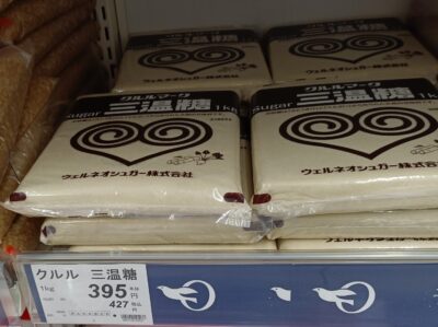 Bags of sanontō, Japanese light brown sugar, displayed with a price tag at a Japanese supermarket