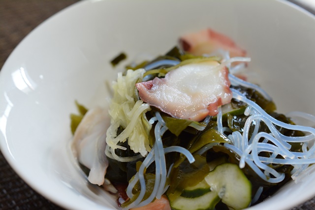 Japanese sunomono salad with octopus, cucumber, wakame seaweed, and glass noodles in a white bowl.