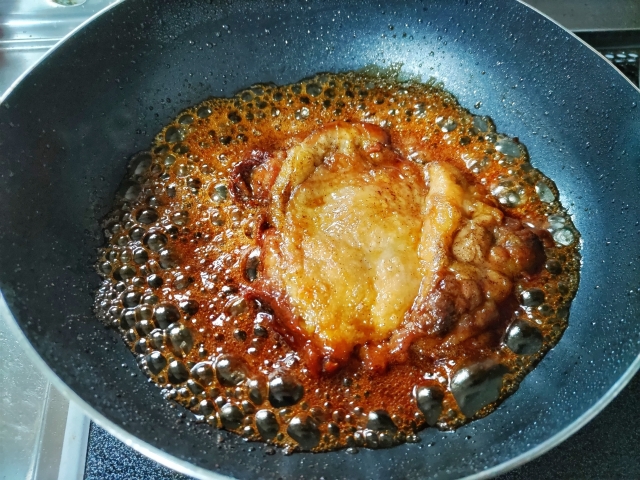 Chicken cooking in a glossy sweet-savory teriyaki-style glaze in a frying pan.