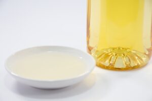 Pale golden Japanese mirin in a small white dish beside a bottle of mirin